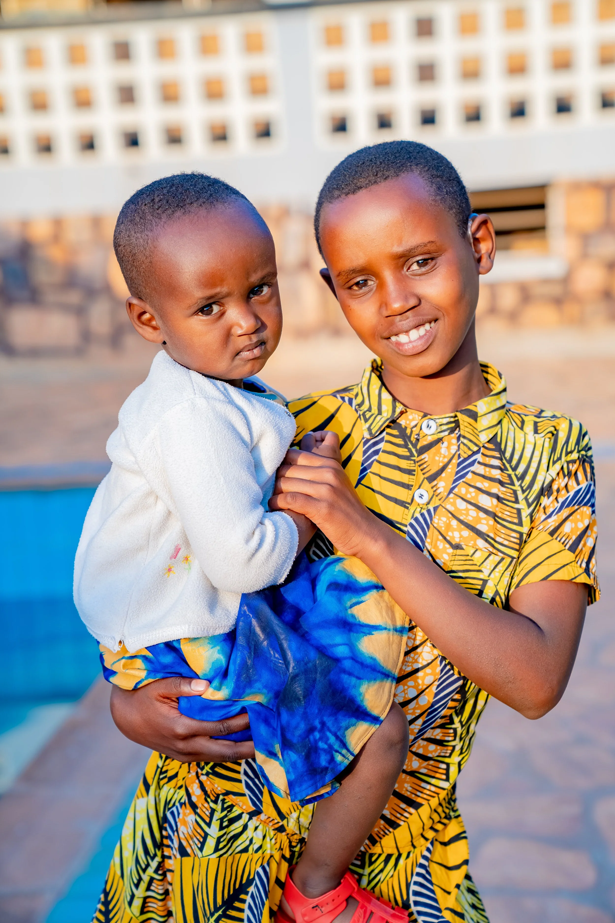 Belyse, 12, carries her younger sister at Butare Center for the Deaf. With digital hearing aids programmed to suit her level of hearing loss, she can now communicate better with her family members and play with her friends in the community and at school.