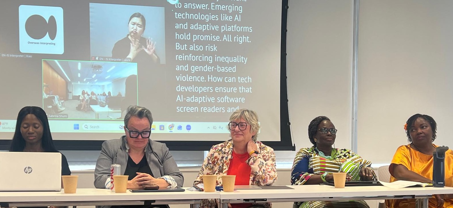 Five diverse female panelists sitting behind a long conference table with laptops and paper cups. A large projector screen behind them displays text reading in part, "Emerging technologies like AI and adaptive platforms hold promise... But also risk reinforcing inequality." The screen also includes inset video feeds featuring a live sign language interpreter and a remote participant.