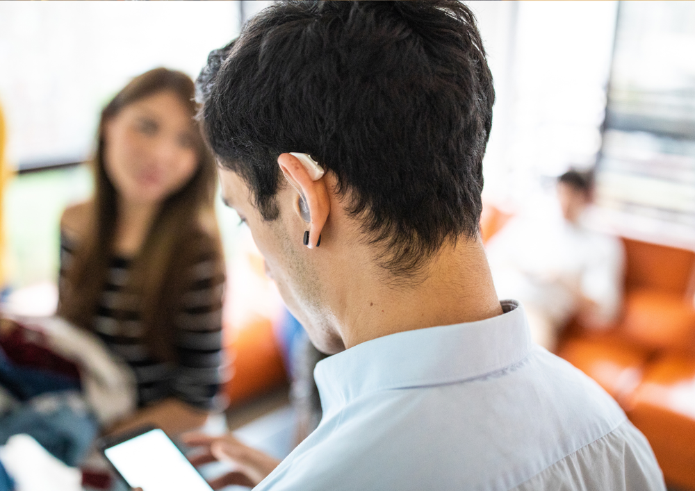 Person wearing a hearing aid looks at a smartphone while talking with others.