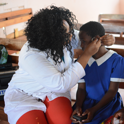 An adult helps a child adjust a hearing aid while another person looks on
