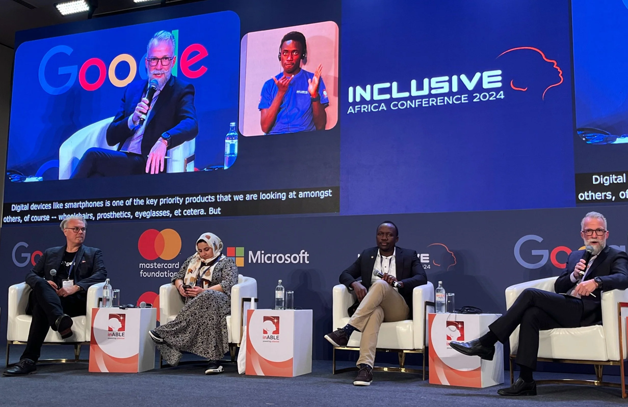 Panel discussion at the Inclusive Africa Conference 2024, with four speakers seated on stage and a sign language interpreter shown on a large screen behind them.