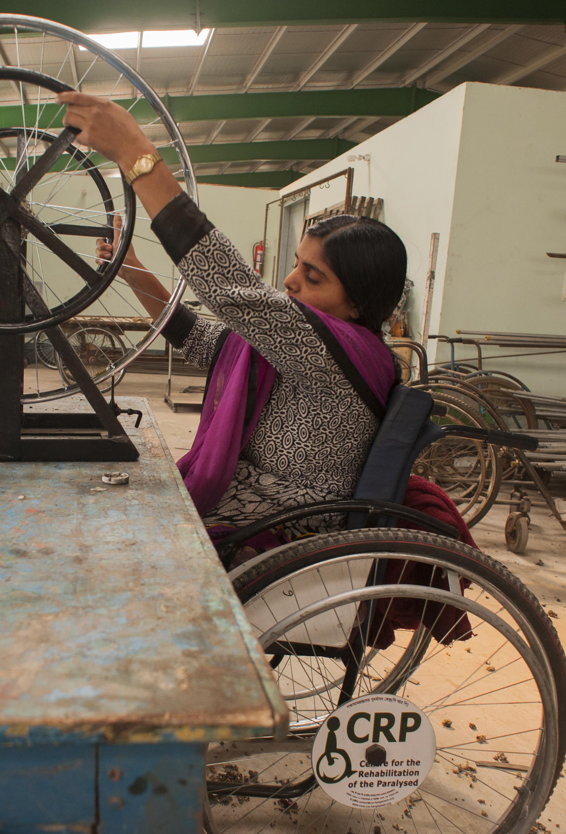 Woman using a wheelchair works in a workshop, adjusting a wheelchair wheel on a repair stand