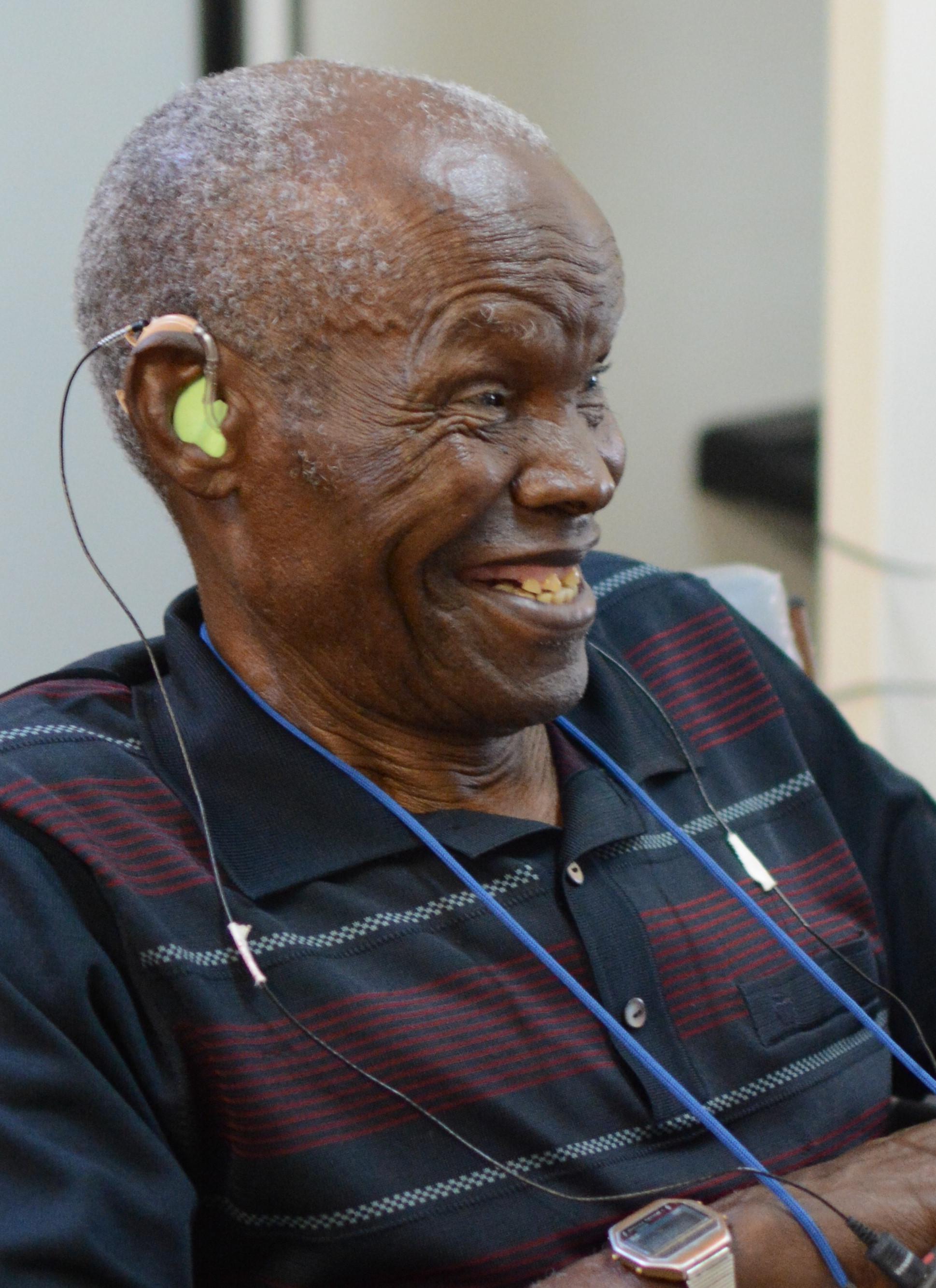 Older man smiling while wearing a hearing aid during a hearing test in a clinic