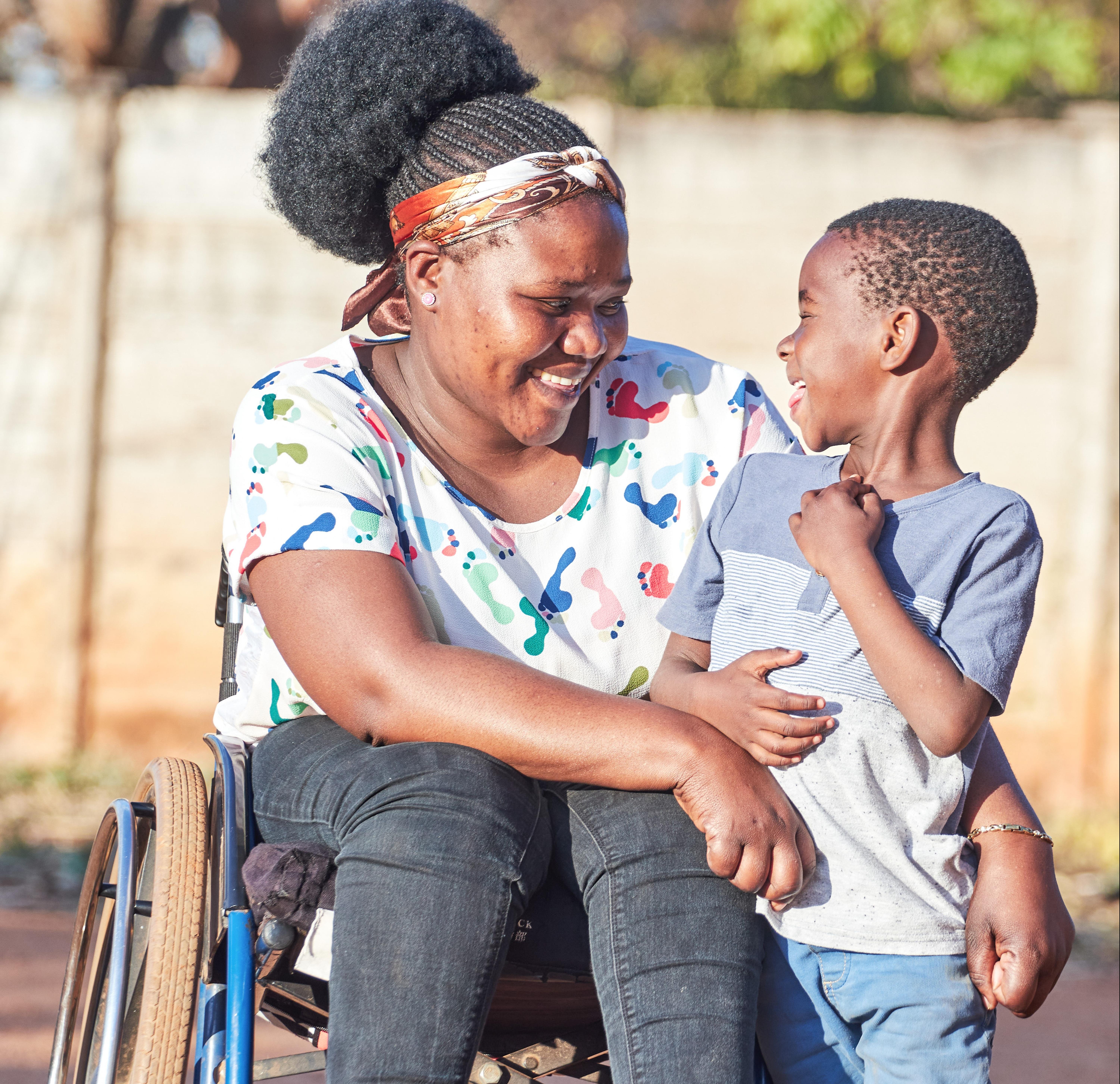 A woman using a wheelchair smiles and talks with a young child outdoors