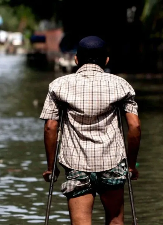 Person using crutches walks through a flooded street, navigating high water after heavy rains