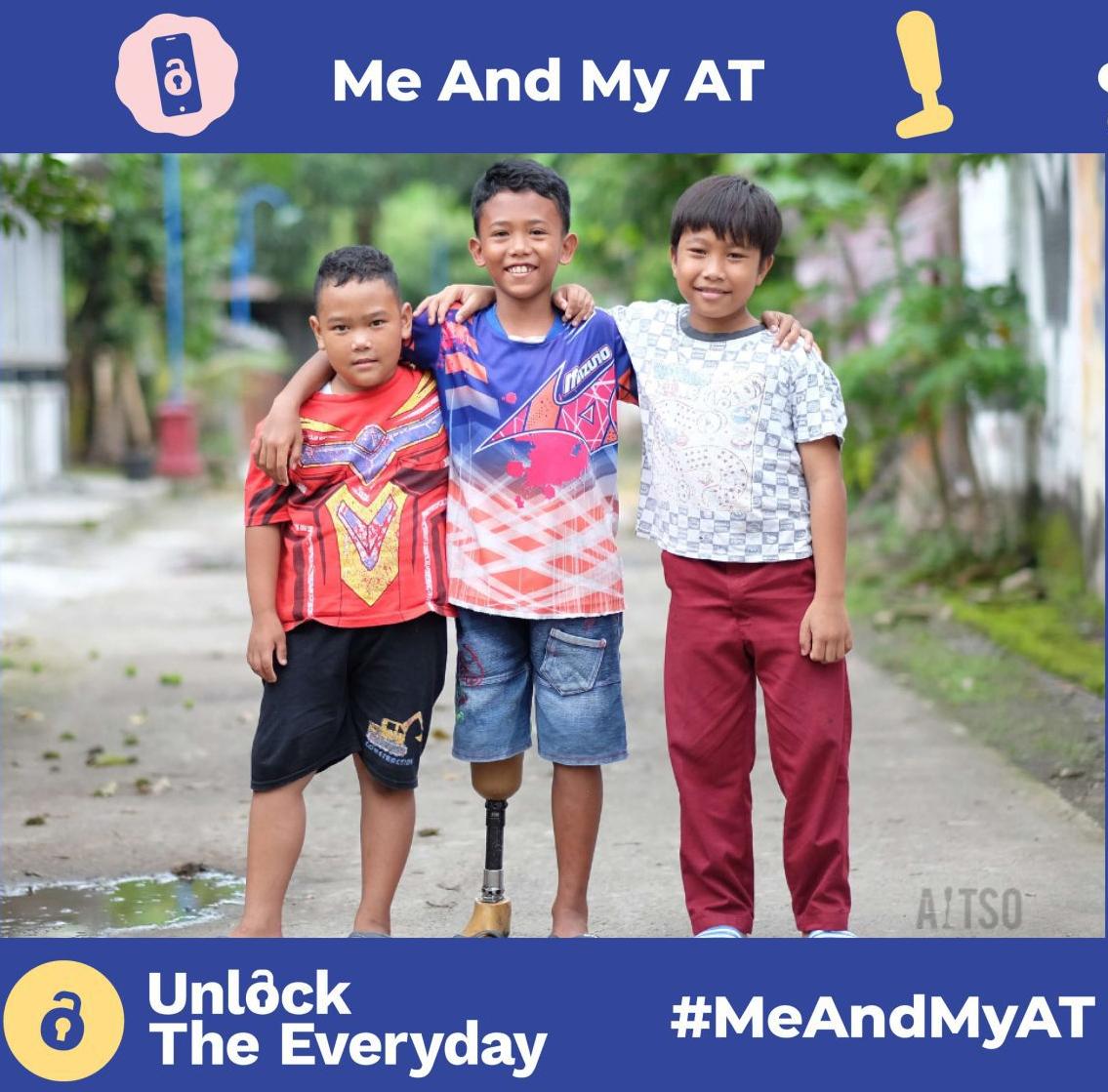 Three children stand outdoors with their arms around each other, smiling; one child uses a prosthetic leg, with ‘Me and My AT’ and ‘Unlock the Everyday’ campaign branding.