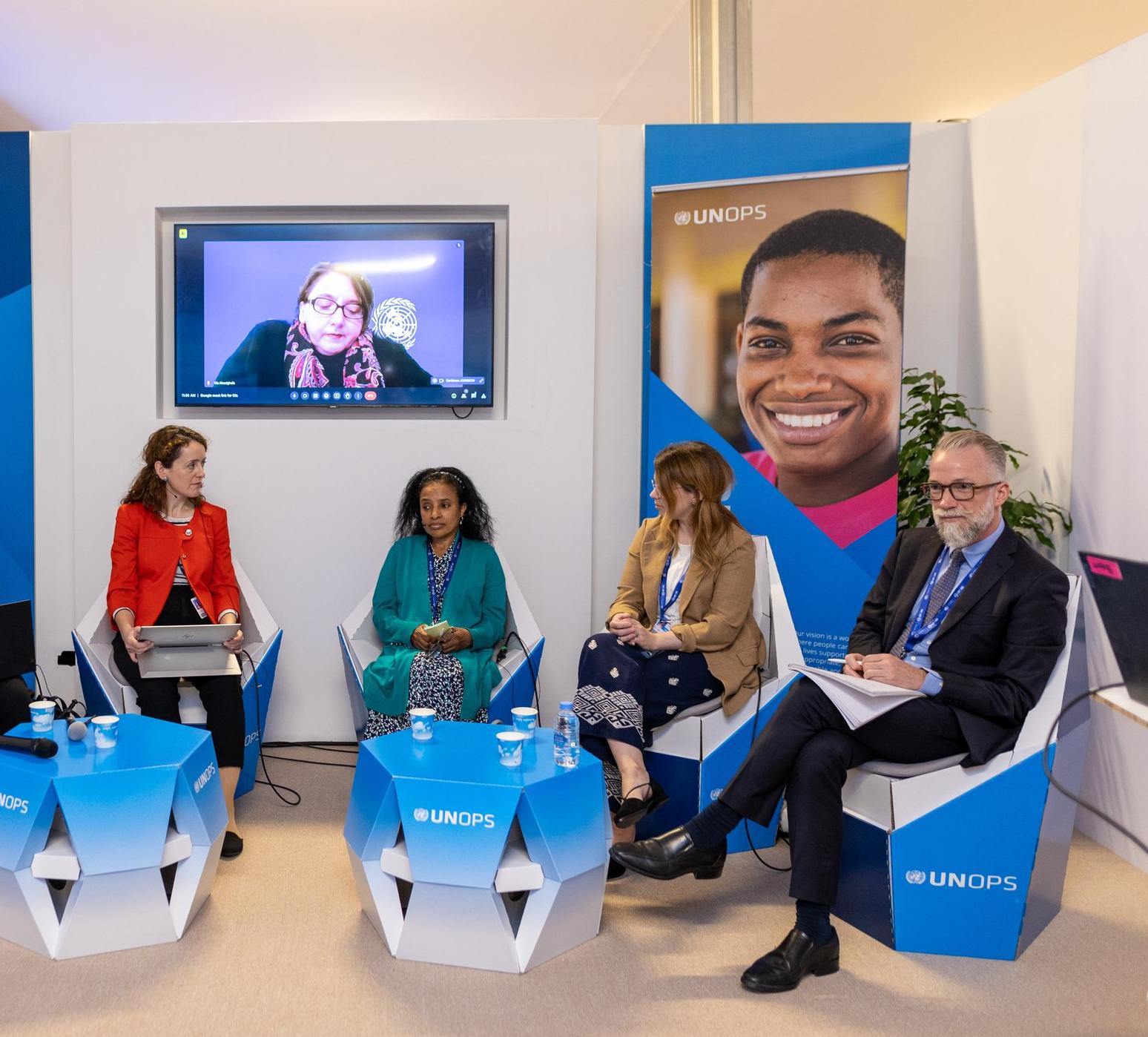 Panel discussion on assistive technology at a UNOPS event, with five speakers seated on stage and one participant joining remotely on screen.