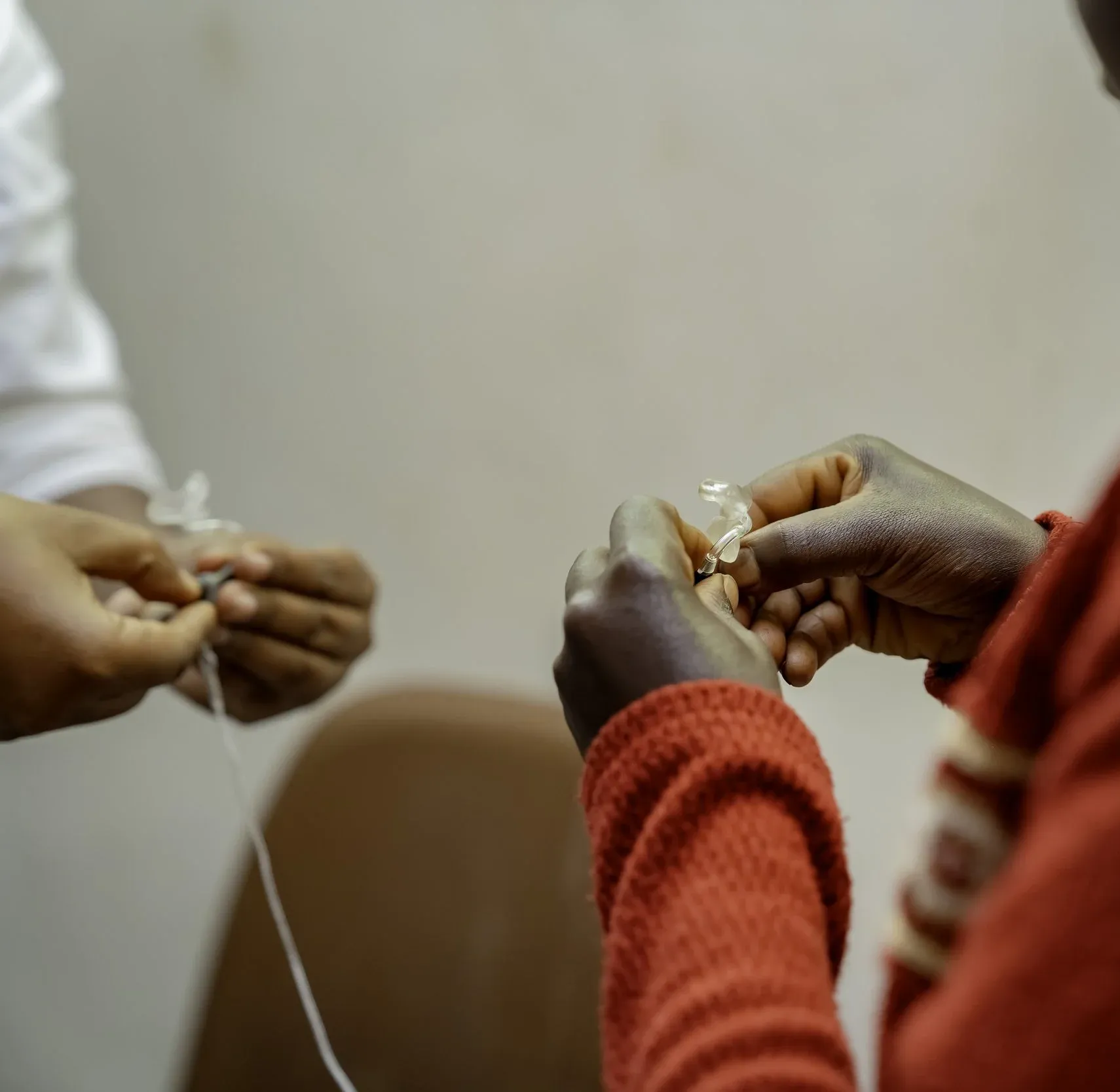 “Close-up of hands fitting or adjusting a small hearing device, with assistance from another person.