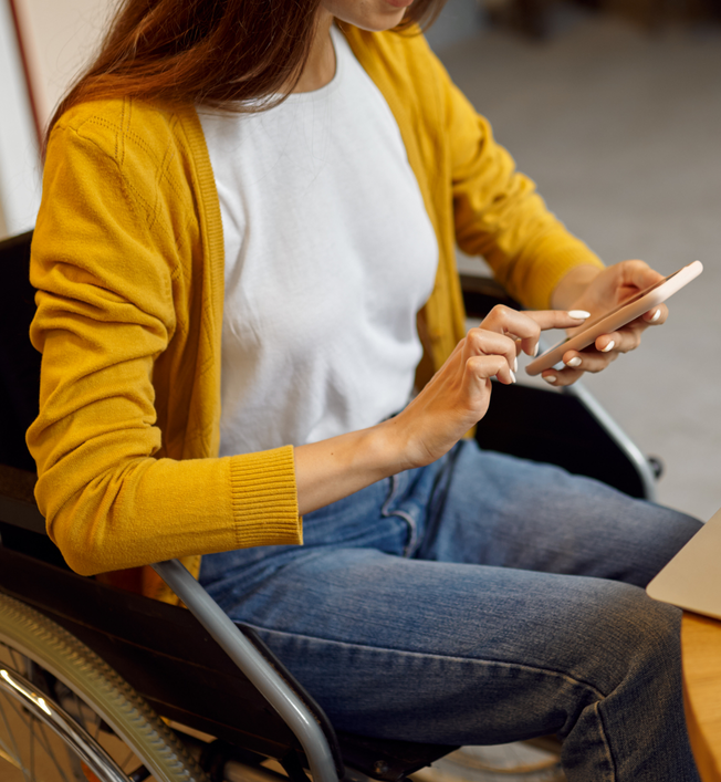 Person seated in a wheelchair using a smartphone at a desk