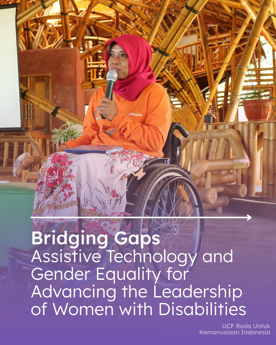 A woman using a wheelchair speaks into a handheld microphone while seated inside a large bamboo-structured building. She wears an orange shirt, a pink headscarf, and a floral skirt, with a notebook on her lap. The image is overlaid with the text: “Bridging Gaps: Assistive Technology and Gender Equality for Advancing the Leadership of Women with Disabilities.” The setting suggests a workshop, meeting, or advocacy event focused on disability inclusion and leadership.