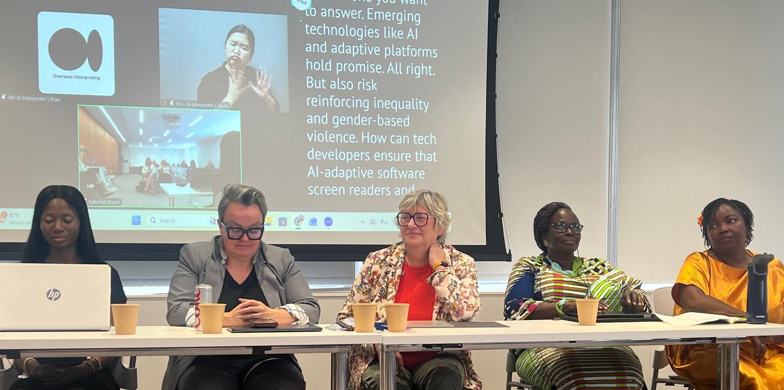 Five diverse female panelists sitting behind a long conference table with laptops and paper cups. A large projector screen behind them displays text reading in part, "Emerging technologies like AI and adaptive platforms hold promise... But also risk reinforcing inequality." The screen also includes inset video feeds featuring a live sign language interpreter and a remote participant.