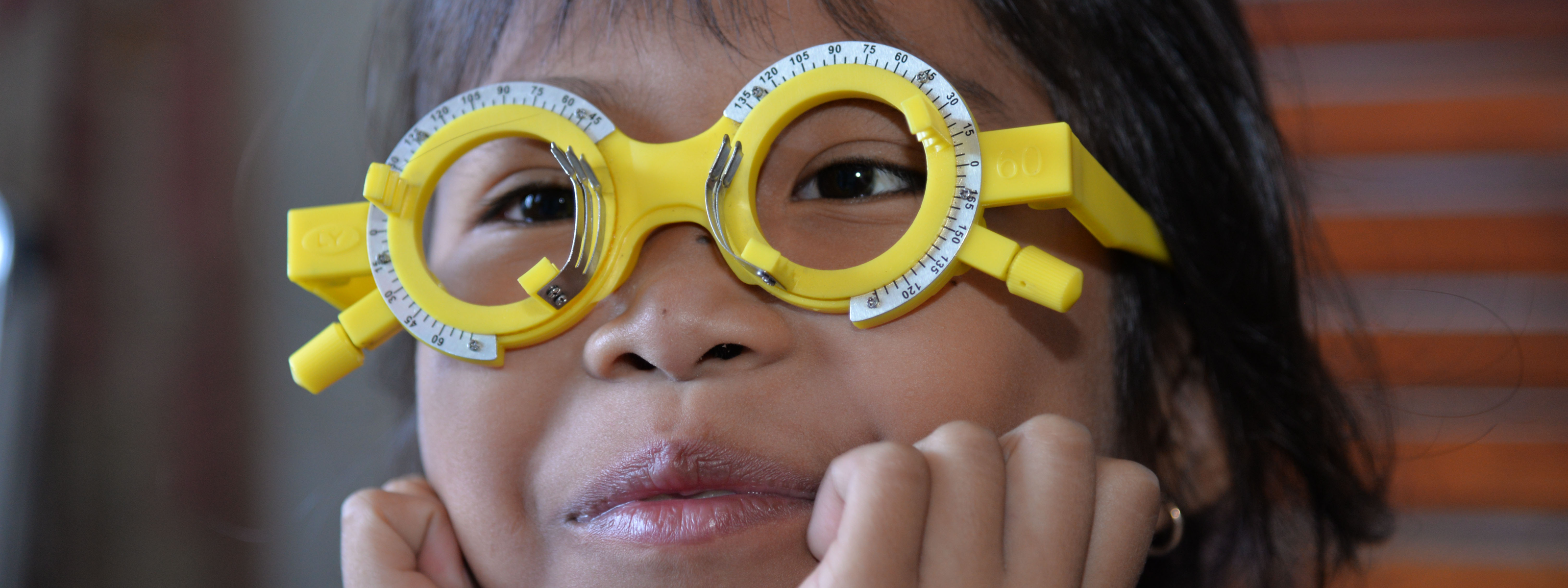 Close-up of a child wearing yellow trial frames during an eyes examination