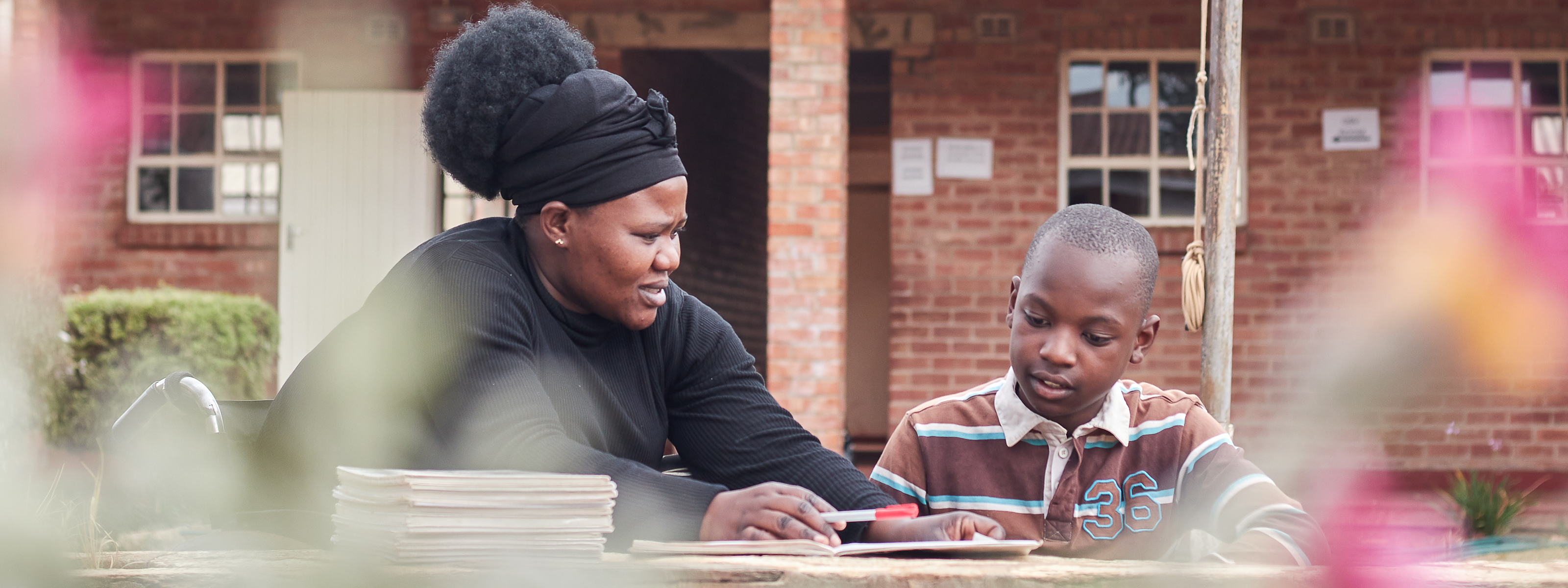 An adult and a child sit together outdoors reading and looking at books.